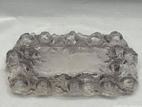 Rectangular pressed glass tray with raised rosebuds and leaf decoration on the border, showing its light lavender tint under lighting.
