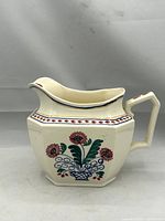 Side view of antique ceramic water pitcher with floral decoration and geometric top border.