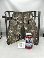 Open hinged metal chocolate mold showing the left and right sides depicting full-bodied standing bunnies, with a soda can for scale.