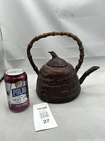 Front angled view showing the teapot's body, bamboo handle, spout, and bird-shaped lid with visible aged patina. A soda can is shown for size reference.