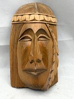 Front view of the carved cedar wood plaque showing the stylized face with feather and headband detail.