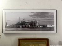 Framed grayscale panoramic photo of the Domino Sugar factory, signed by Brian Wallace, hanging on a wall, showing full view of the frame and image.