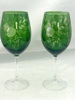 Pair of green cut-to-clear etched wine glasses with clear stems, upright on a neutral background.