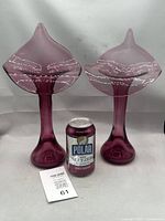 Pair of cranberry-colored glass vases with a soda can between them for scale, showing their translucent and elegant tall shapes with flared rims.