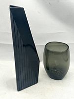 Front view of the black angular ceramic vase with matte striping and the shorter smoke glass vase side by side on white background.