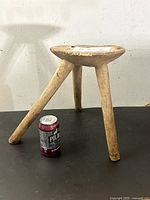 Front angled view of the rustic wooden stool showing three legs and irregular carved seat with a beverage can for scale.