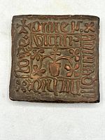 Front view of the antique red clay tile with its medieval-style inscriptions and central floral motif.