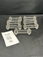 Seven clear pressed glass utensil rests laid out on black background forming two groups plus one