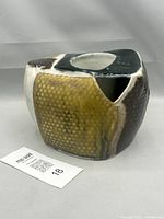 Studio pottery vessel 3/4 view showing textured ochre front panel with dark glaze sides and asymmetric opening