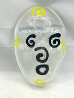 Top-down view of clear glass abstract face sculpture with visible black and yellow spiral and wave motifs.