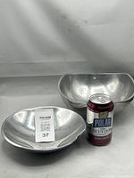 Two vintage Nambe alloy bowls shown together on a white backdrop. Front bowl is Nambe Classic 527 tri-corner form, back bowl is Nambe Spiral 628 with curved spiral design. A soda can is placed next to the bowls to show scale.