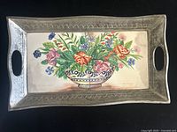 Front view of the rectangular tray showing colorful floral painted ceramic tiles inside an embossed tin frame with handles on both sides.