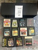 Top view of 11 Atari 2600 cartridges arranged in three rows beside the black vertical plastic game cartridge storage case.
