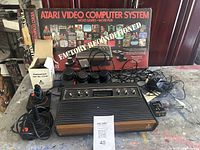Atari 2600 system with woodgrain panel, visible CX-40 joysticks, paddle and driving controllers, power supply cables, original box marked 'Factory Reconditioned'.