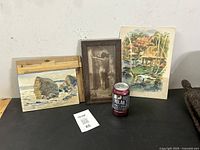 Three items displayed: framed sepia print, signed watercolor with coastal scene, mid-century dinner menu with tropical artwork, soda can for scale.