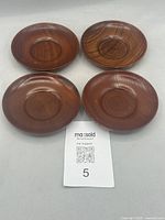 Top-down view of four vintage wooden Japanese Chataku saucers arranged in a square formation showing wood grain and size relative to a MaxSold ticket.