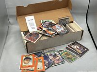 Photo of open cardboard box filled with assorted sports trading cards, some loose and some stacked in piles.