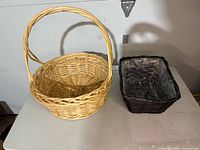 Photo showing two baskets side by side: round natural wicker basket with handle and rectangular dark basket with plastic liner inside.