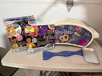Easy Bake Oven with dough mixes, blue spatula tool, and white tray on white surface photographed from side view.