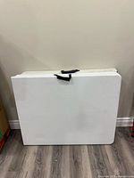 Photo of the table folded in half, showing the white surface and black carry handle on top.