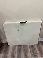 Folded rectangular white table with handle showing stains and wear marks.