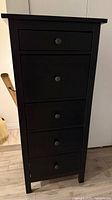 Front view of the black 5-drawer IKEA Hemnes dresser showing the five evenly spaced drawers and round knobs.