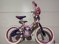 Side view of pink and purple Disney Princess kids bicycle showing white tires and pink rims, glittery purple seat, and Disney Princess decals on frame.