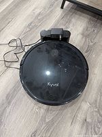 Top view of the Kyvol robot vacuum showing its round black body and logo, placed on the floor near its charging dock.