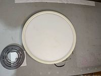 Top view of round white ceiling light diffuser cover and control module on a flat surface.