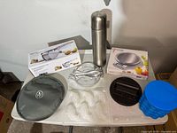 Photo of all items in lot showing thermos, potato ricer, food scale, burger press, ice mold, keep warm cover, and fish mold tray.