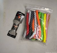 Photo showing a sealed bag containing multiple pairs of colorful no tie coil shoe laces in various colors plus one packaged pair of adult gray flat shoe laces by So Sole.