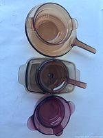 Top view of three amber glass bakeware items showing two handled round pot, rectangular casserole, and round covered casserole dish.