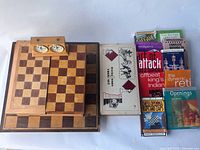 Overview shot of two wooden chess boards stacked with a chess clock on top and a collection of chess books to the side, showing condition and lot contents.