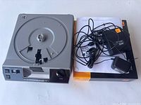 Kodak Ektagraphic III slide projector with power cord and remote control placed next to a box.