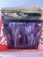 Top view of milk crate containing multiple stained glass sheets in various colors and textures, some wrapped in newspaper.