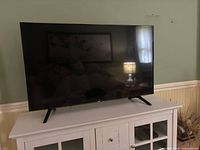 Front view of 50 inch flat screen TV on white cabinet with the screen turned off reflecting room details