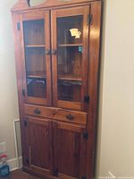 Photo of light wood corner china cabinet showing upper glass panel doors, two drawers with handles, and lower solid wood doors with hinges.