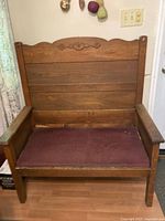 Wooden deacon's bench with cushioned seat and carved decorative backrest.
