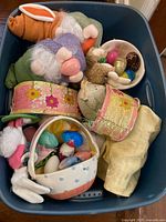 Top-down photo showing various Easter and spring decorations stored in a blue plastic bin including plush bunnies, ribbons, artificial birds, a fabric piece, and a bowl of colorful eggs.
