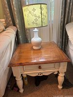 End table with white painted carved legs and natural wood top, holding a white ceramic table lamp with a floral pattern lampshade.