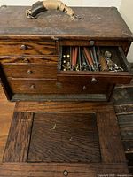 Wooden leather working toolkit box with drawers open showing multiple leatherworking tools such as stitching awls, punches, and other tools inside.
