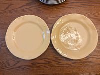 Photo of two cream-colored plates, one plain and one embossed with a textured rim, placed on a wooden surface.