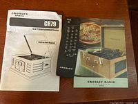 Instruction manuals for Crosley CR79 Entertainment Center and remote control on table.
