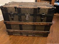 Front view of vintage dark wood steamer trunk showing metal reinforcements, central lock, and latch hardware.