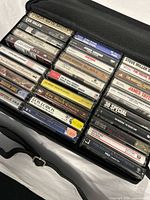 Photo of 30 classic rock cassette tapes in clear plastic cases inside a black nylon carrying bag with zipper closure and carrying strap.