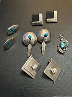 Top-down photo showing all four pairs of earrings and the turquoise stone pendant displayed on black fabric background.