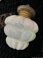 Side view of entire swag lamp showing pearl iridescent multi-lobed glass shade and brass fixture.