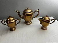 Full set of three vintage brass tea set pieces: teapot, creamer, and sugar bowl on white surface