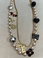 Full view of the double strand pearl and gold-tone chain necklace featuring multiple Minnie Mouse-themed charms including ears with red bow, LOVE letters, and a red and black charm.