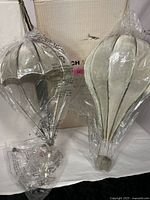 Both the hot air balloon and parachute lighting fixtures seen from front and side angles, still wrapped in plastic and set in front of their original box